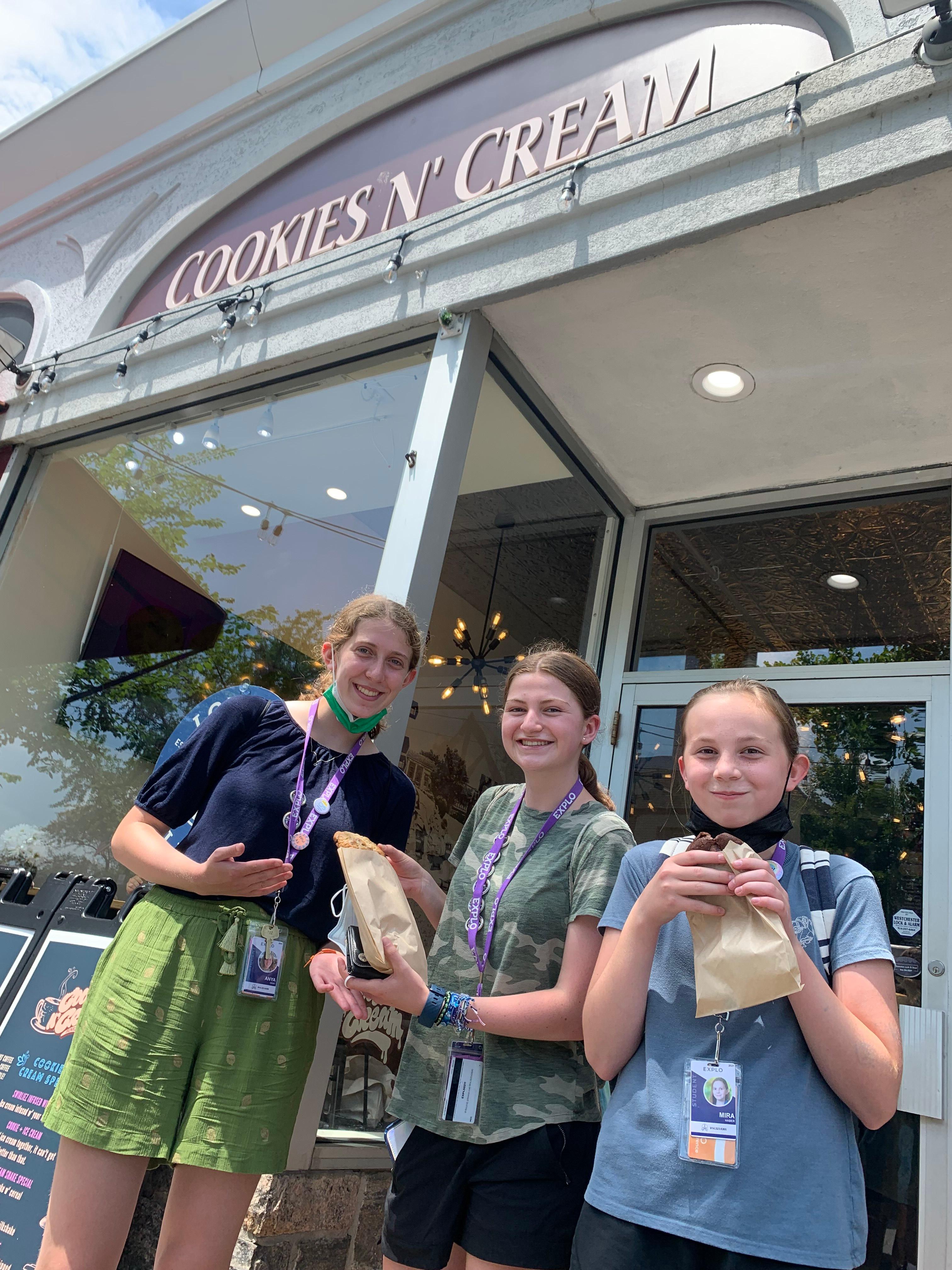 Three female EXPLO students stand side by side, treats in hand, in front of Cookies N' Cream in Bronxville, NY.
